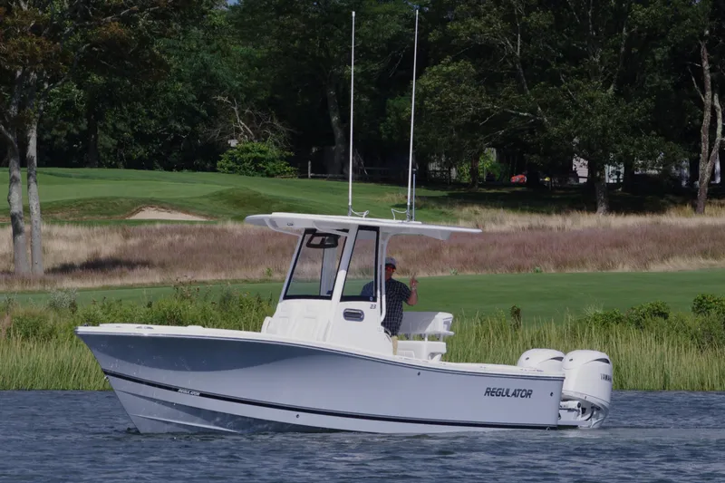 Slide: The Image of 2024 Regulator 23 boat cruising on a serene lake with lush greenery. - 6