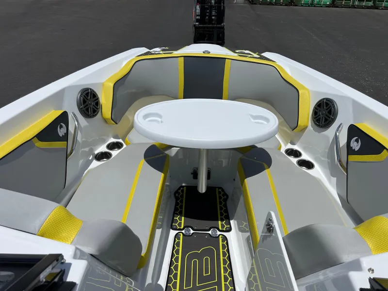Slide: The Image of 2023 Scarab 255 Wake ID boat interior with yellow and gray seating, round table, and speakers. - 15