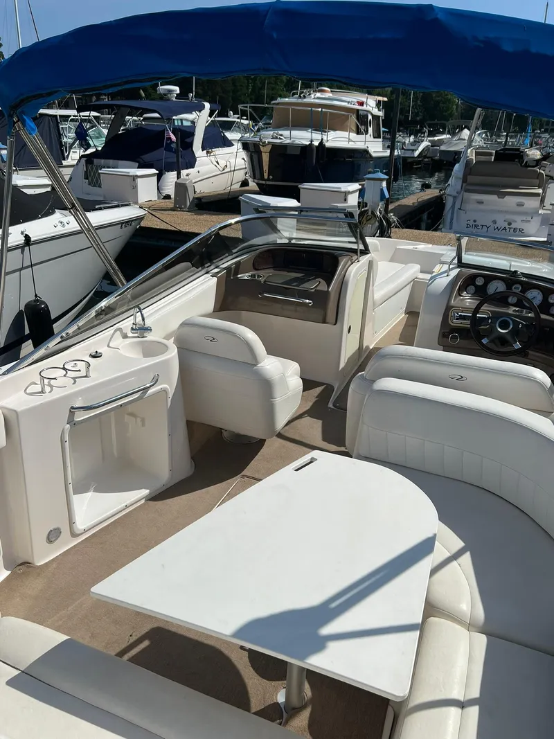 Slide: The Image of 2006 Regal 2600 Bowrider with blue canopy, docked at marina, featuring spacious seating and table. - 14