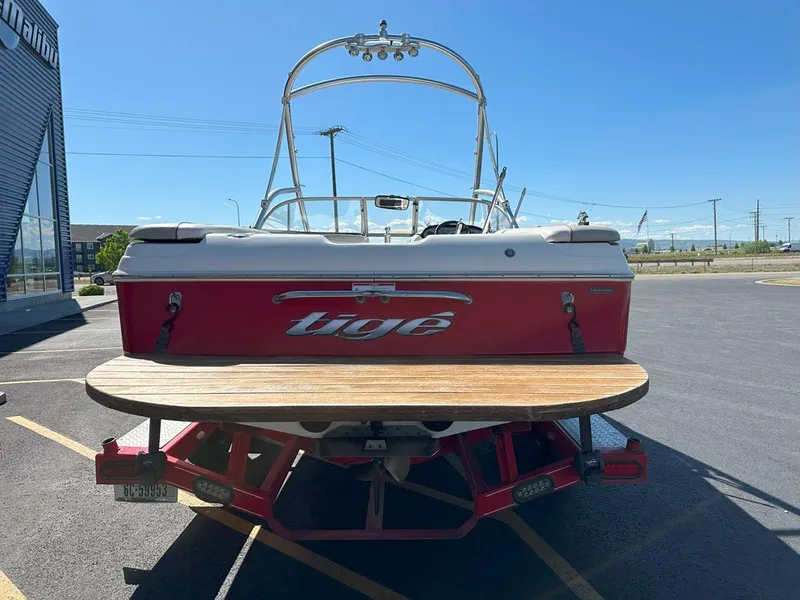 Slide: The Image of 2006 Tigé 22i boat, red and white, parked on a trailer in a sunny lot. - 8
