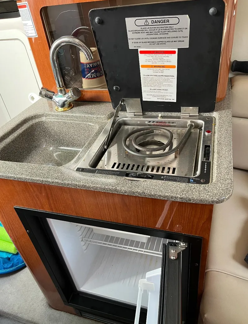 Slide: The Image of 2002 Crownline 242 CR boat kitchenette with sink, stove, and mini-fridge. - 4
