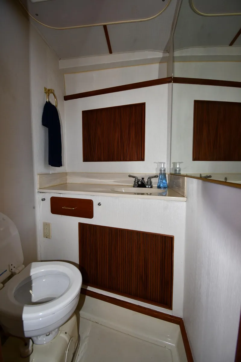 Slide: The Image of 1988 Tollycraft 34 Sundeck bathroom with toilet, sink, and wooden cabinetry. - 35
