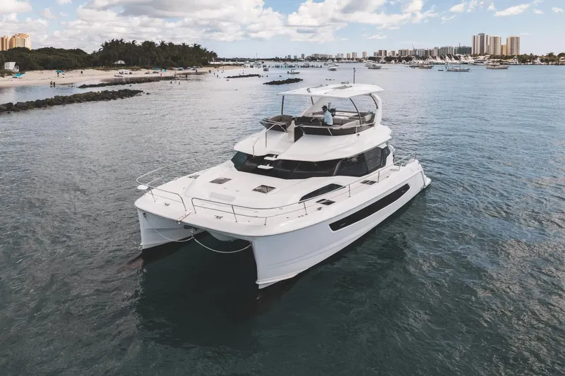 Slide: The Image of 2024 Aquila 44 Yacht cruising near a scenic beach with palm trees and city skyline. - 37