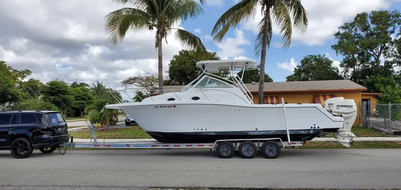 Slide: The Image of 2000 Pro-Line 29 Walkaround boat on trailer, parked beside a black SUV, under palm trees. - 1