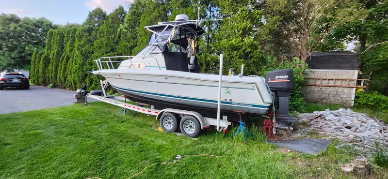 Slide: The Image of 1999 Stamas 250 Express boat on trailer, parked on grass near trees and a driveway. - 20