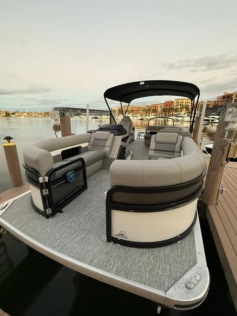 Slide: The Image of 2024 Premier Sunsation 230 RE pontoon boat docked at a scenic marina. - 14
