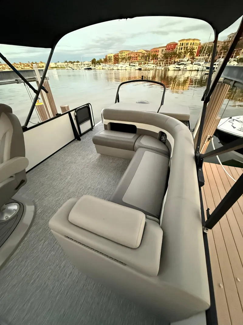 Slide: The Image of 2024 Premier Sunsation 230 RE boat interior with plush seating, docked at a scenic marina. - 19