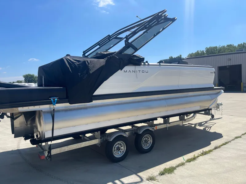 Slide: The Image of 2024 Manitou Cruise pontoon boat on a trailer in a sunny outdoor setting. - 5