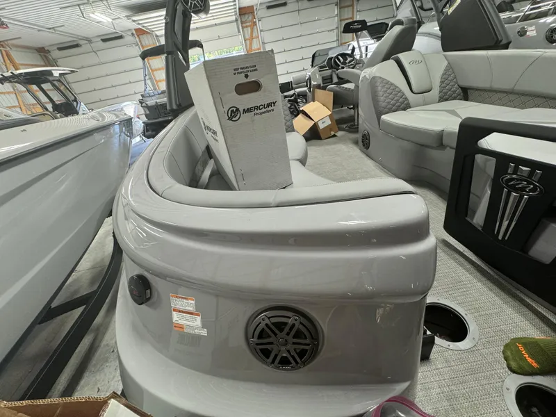 Slide: The Image of 2024 Manitou 25 LX RF boat interior with gray seating and Mercury box in a showroom. - 13