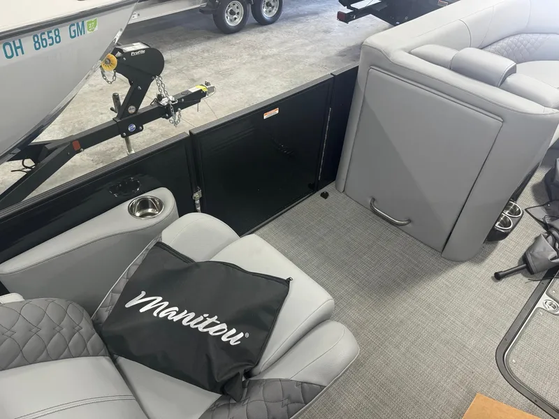 Slide: The Image of 2024 Manitou 25 LX RF boat interior with gray seating and Manitou-branded bag. - 8