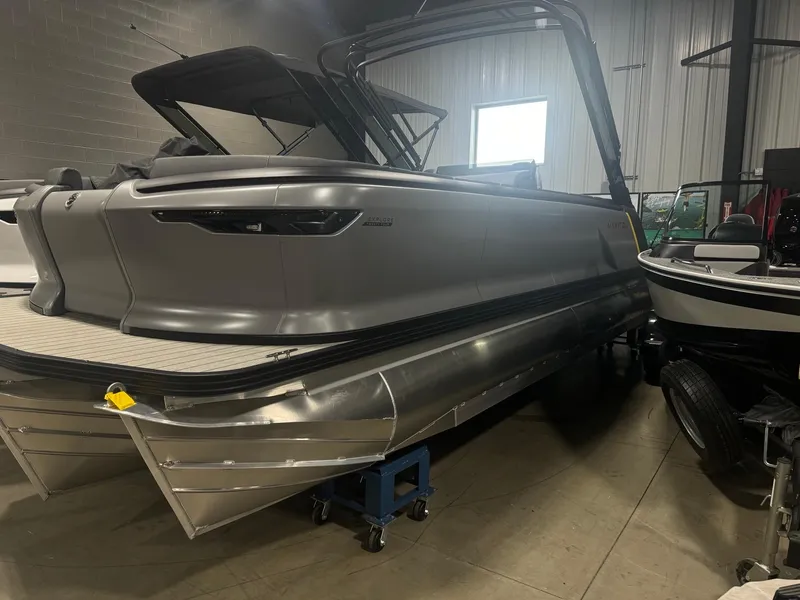 Slide: The Image of 2024 Manitou Explore pontoon boat in showroom, sleek design, metallic finish. - 0