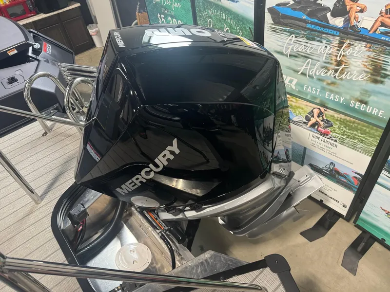 Slide: The Image of 2024 Manitou Explore boat with Mercury engine, showcased indoors with promotional banners. - 13