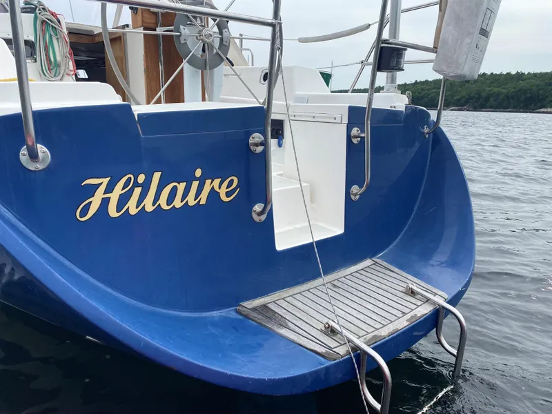 Slide: The Image of Blue Freedom 35 sailboat named "Hilaire" with a swim platform, docked on calm water. - 20