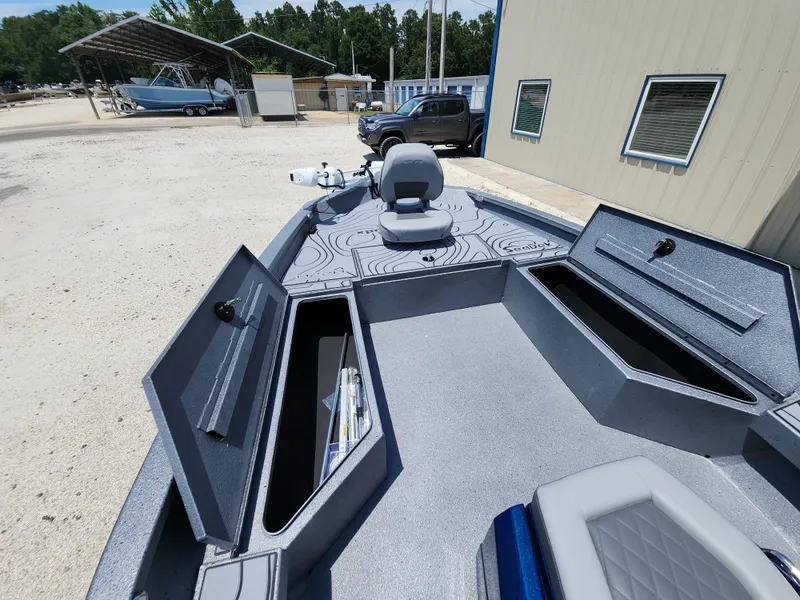 Slide: The Image of 2025 Xpress H20B boat with open storage compartments and seating, parked outdoors. - 12