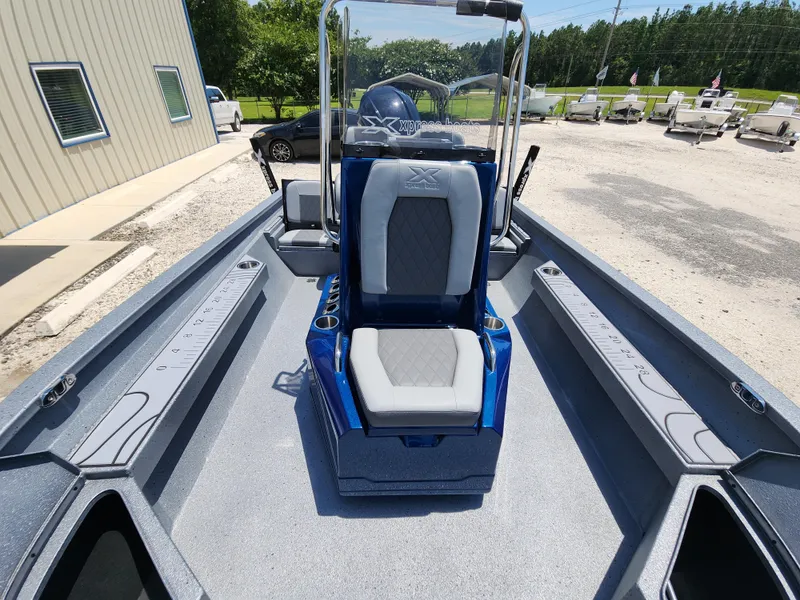 Slide: The Image of 2025 Xpress H20B boat interior with center console and seating, parked outdoors. - 13