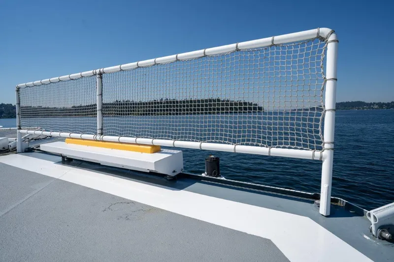 Slide: The Image of Dakota Creek 1999 catamaran deck with safety netting, overlooking calm waters and distant shoreline. - 46