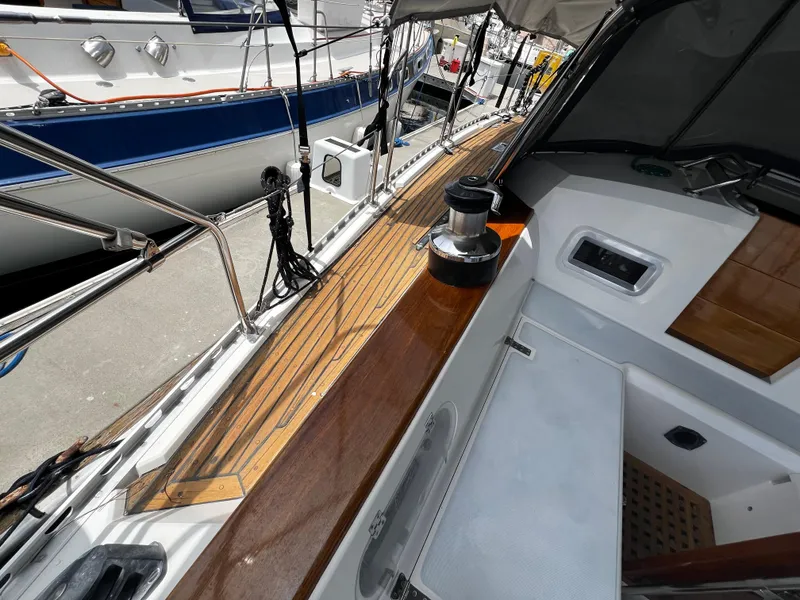 Slide: The Image of 1987 Norseman 400 sailboat deck with wooden finish and winch, docked beside other boats. - 13