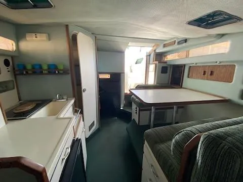 Slide: The Image of Interior of a 1989 Sea Ray '30 Sundancer boat, featuring a compact kitchen and dining area. - 7