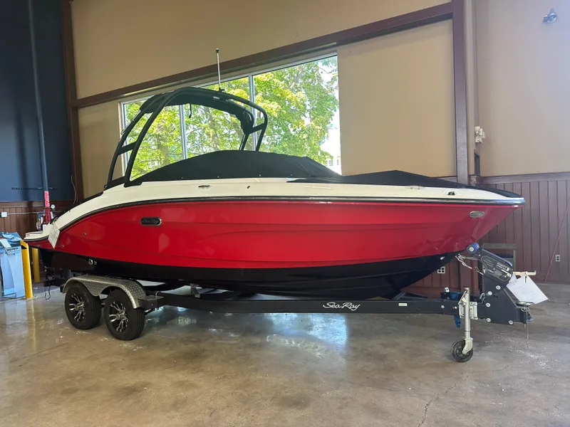 The Image of 2024 Sea Ray SPX 210 boat with red hull on trailer indoors. - 0