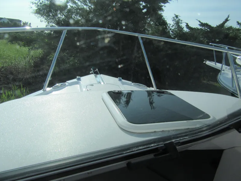 Slide: The Image of 2025 Parker 2420 Sport Cabin boat deck with windshield and hatch, surrounded by greenery. - 14