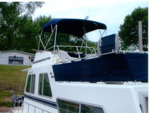 Slide: The Image of 1992 Holiday Mansion houseboat with blue canopy, docked near a grassy area and trees. - 13