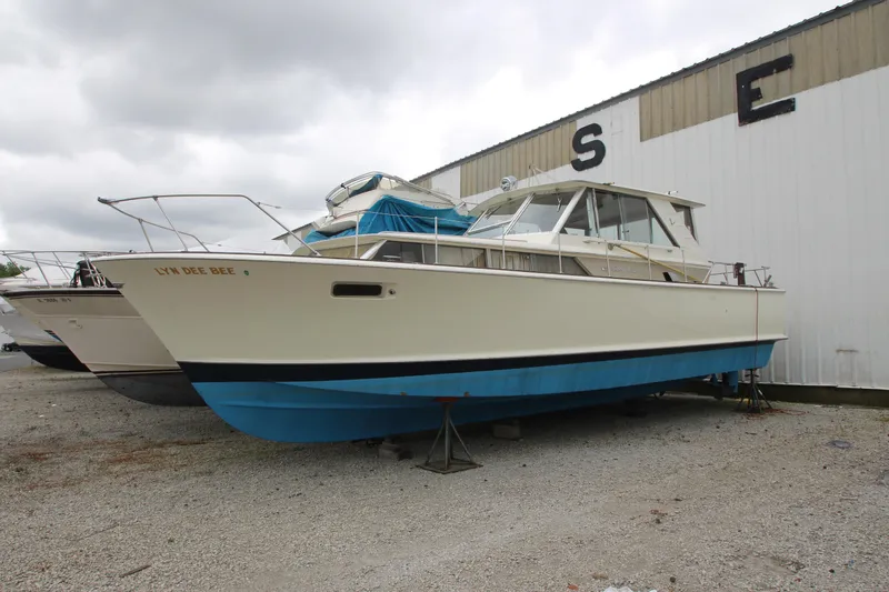 Slide: The Image of 1965 Chris-Craft Commander boat on dry dock, white and blue hull, overcast sky. - 0