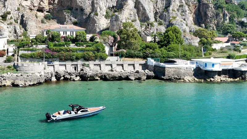 Slide: The Image of Luxury DNA 46 boat cruising near rocky coastline with lush greenery, 2025 model. - 6