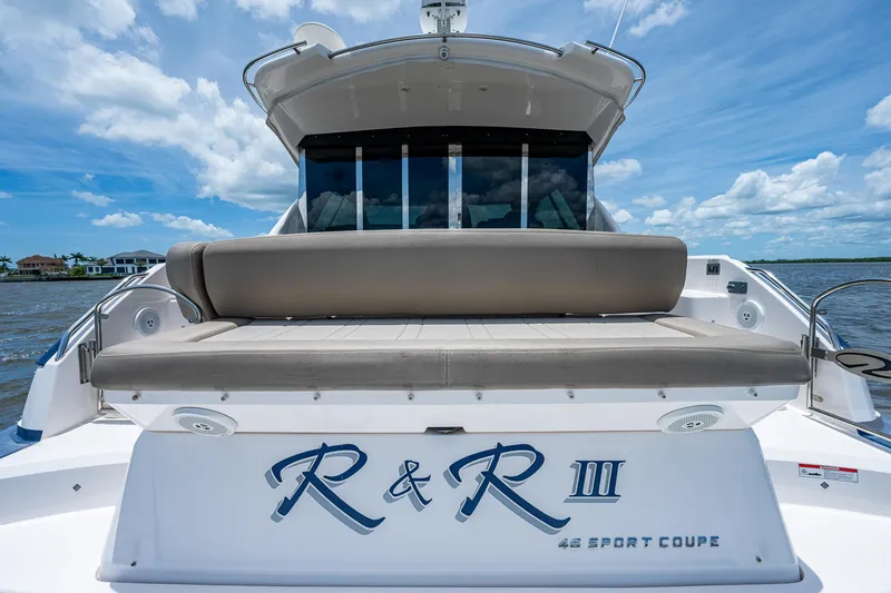 Slide: The Image of 2015 Regal 46 Sport Coupe luxury yacht with cushioned seating, docked on a sunny day. - 19