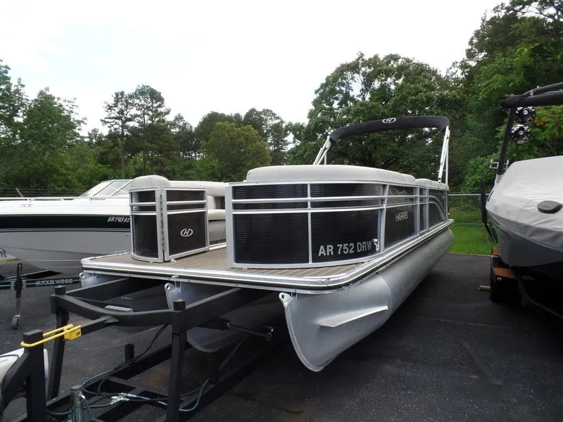 Slide: The Image of 2018 Harris Cruiser 240 pontoon boat on trailer, surrounded by trees and other boats. - 6