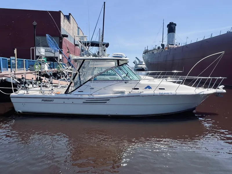 Slide: The Image of 2002 Pursuit 3000 Express boat docked near a large ship, clear sky background. - 2