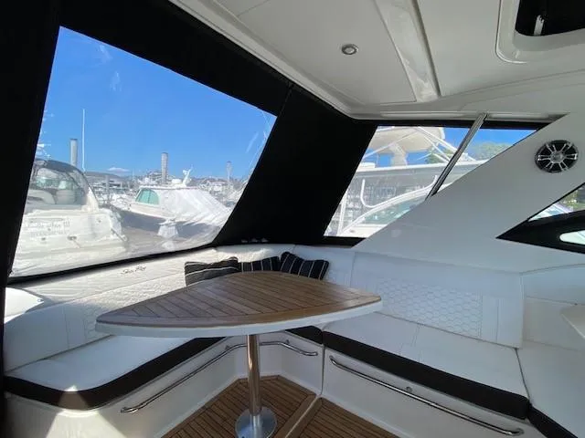 Slide: The Image of 2022 Sea Ray 320 Sundancer Outboard interior with white seating and wooden table. - 11