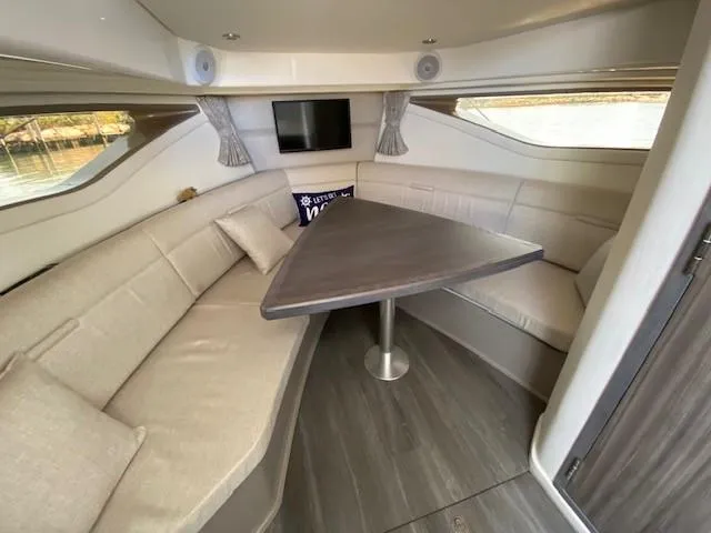 Slide: The Image of 2022 Sea Ray 320 Sundancer Outboard cabin interior with dining area and TV. - 7