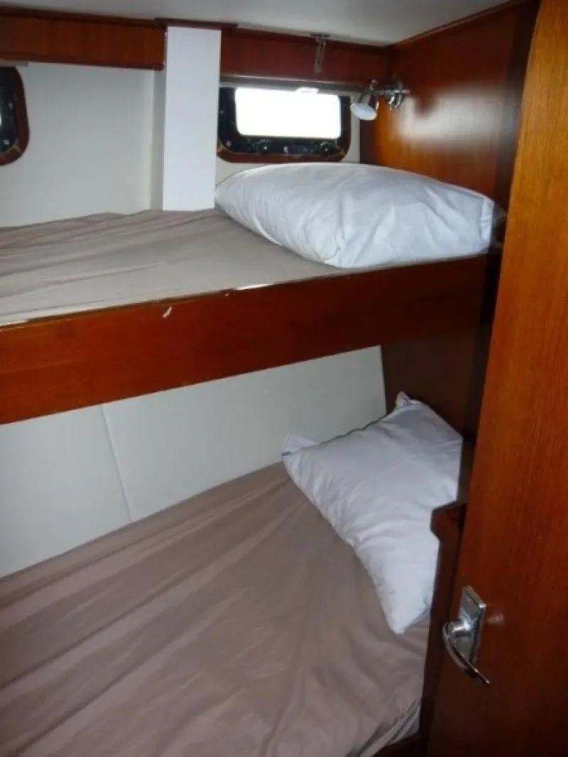Slide: The Image of 1990 Cheoy Lee Sloop cabin with wooden bunk beds and porthole window. - 46