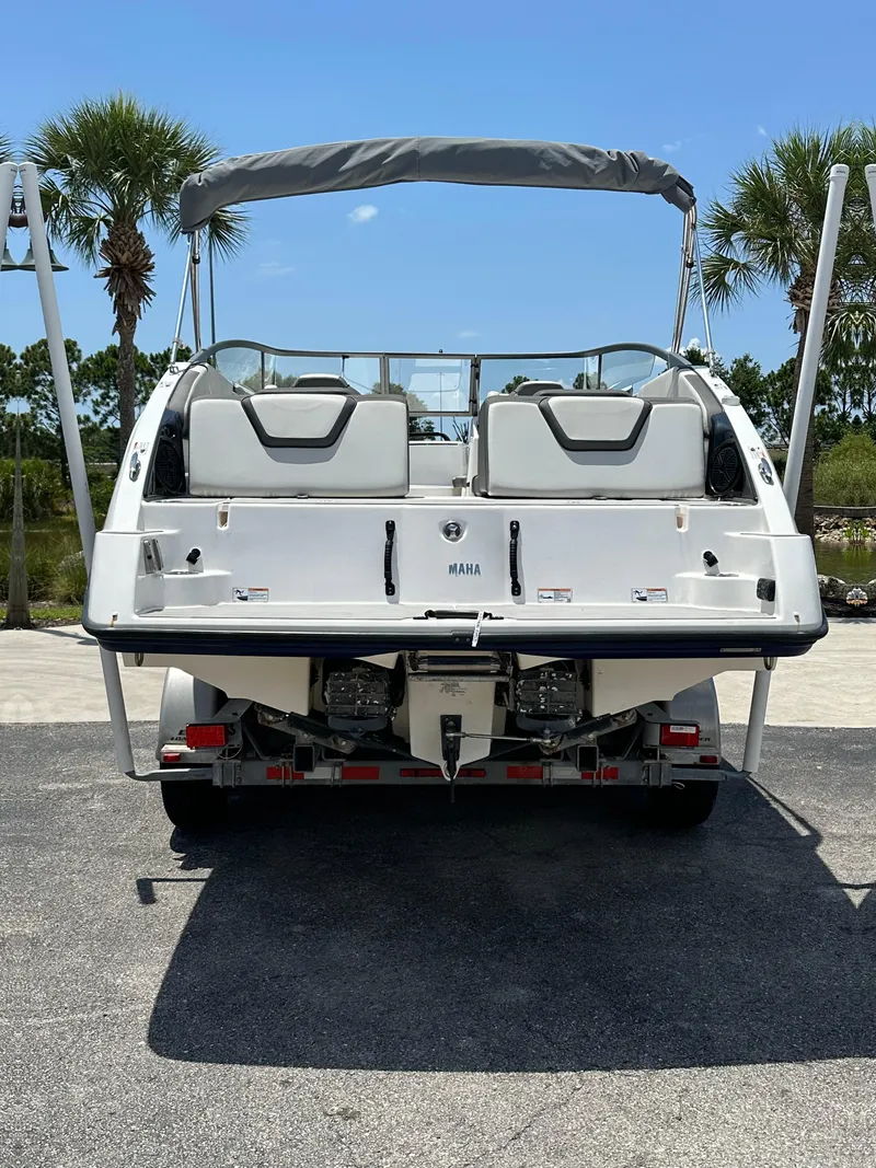 Slide: The Image of 2022 Yamaha Boats SX250, rear view, docked with bimini top, palm trees in background. - 4