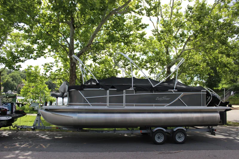 Slide: The Image of 2021 SunChaser Geneva Cruise 24 SB pontoon boat on a trailer, parked under trees. - 0