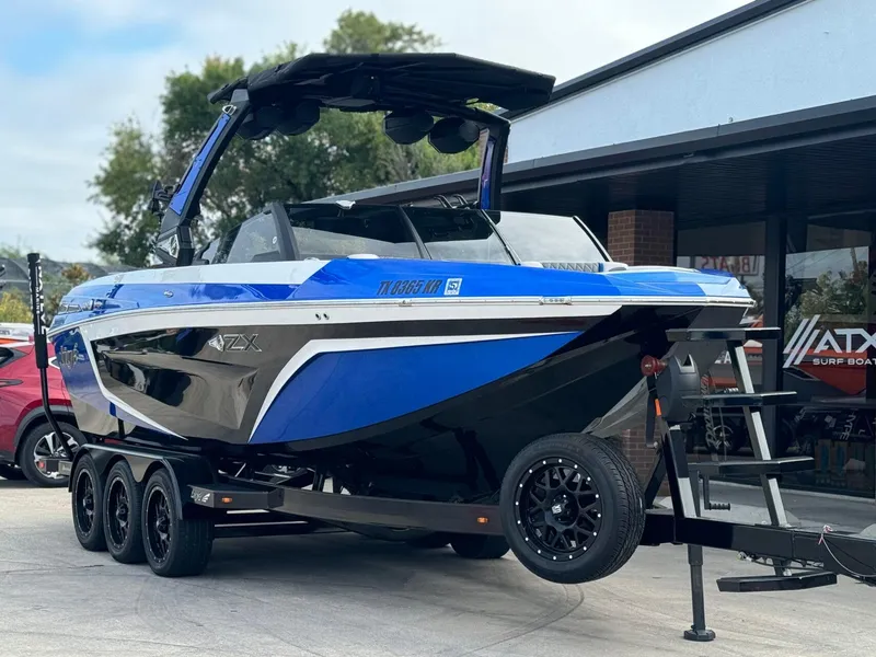 Slide: The Image of 2023 Tigé 25ZX boat on trailer, blue and black design, parked outdoors. - 3