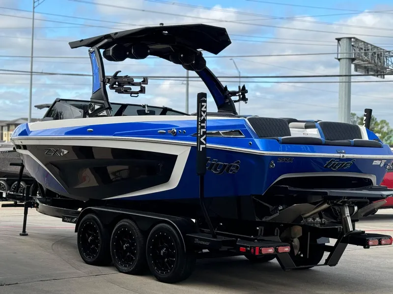 Slide: The Image of 2023 Tigé 25ZX boat in blue and black on a trailer, parked outdoors. - 6