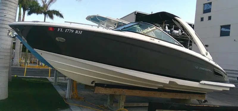 Slide: The Image of 2017 Regal 2800 Bowrider boat on a lift near palm trees and a building. - 0