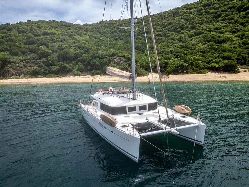Slide: The Image of 2012 Lagoon 560 catamaran anchored near a lush, green island shoreline. - 1