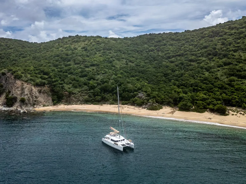 Slide: The Image of Lagoon 560 catamaran anchored near a secluded beach with lush green hills, 2012 model. - 10