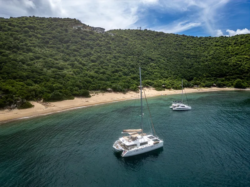 Slide: The Image of Two Lagoon 560 catamarans anchored near a lush, green island coastline. - 14