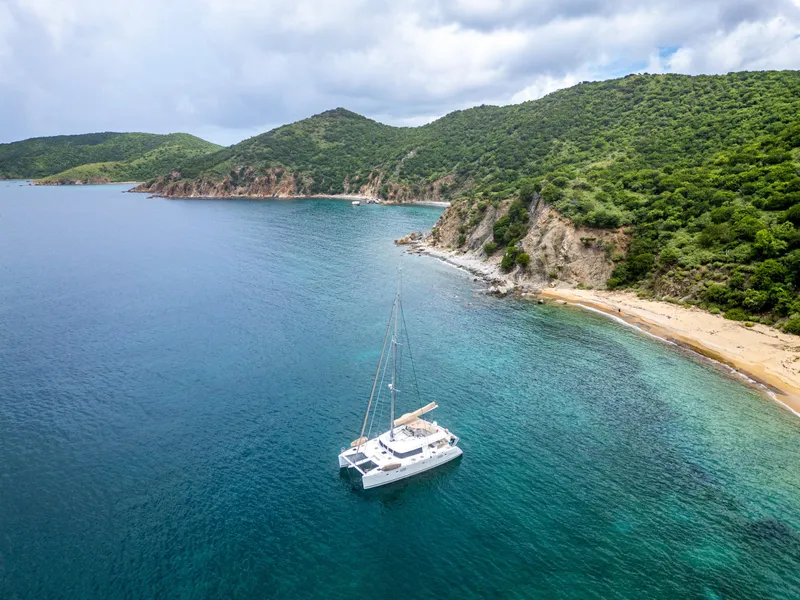 Slide: The Image of Aerial view of 2012 Lagoon 560 catamaran near a scenic coastline with lush green hills. - 5