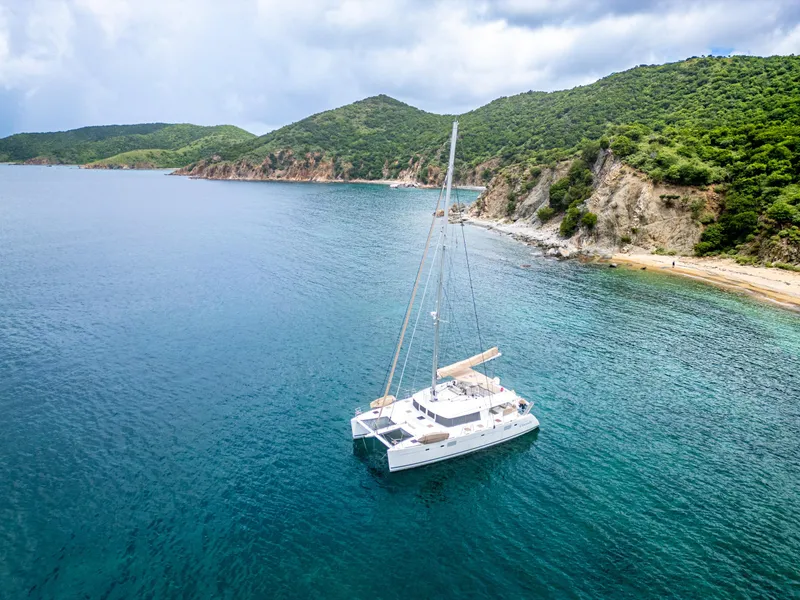 Slide: The Image of 2012 Lagoon 560 catamaran anchored in a serene bay with lush green hills. - 6