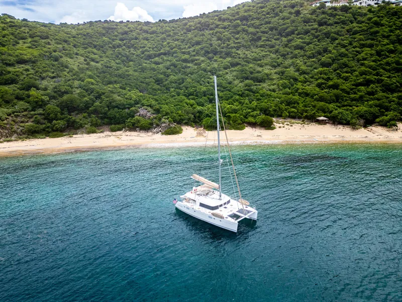 Slide: The Image of Lagoon 560 catamaran anchored near a lush, green coastline and sandy beach, 2012 model. - 7