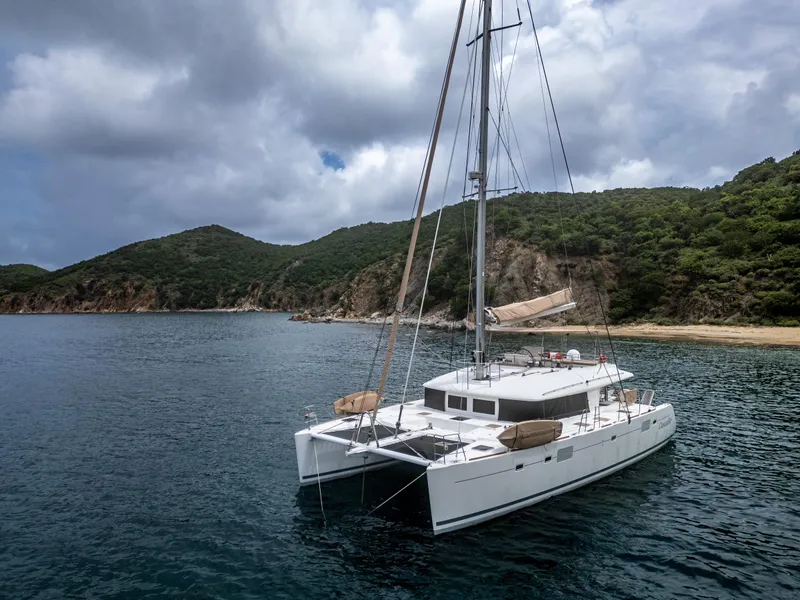 Slide: The Image of Lagoon 560 catamaran anchored near lush, hilly coastline under cloudy skies, 2012 model. - 8