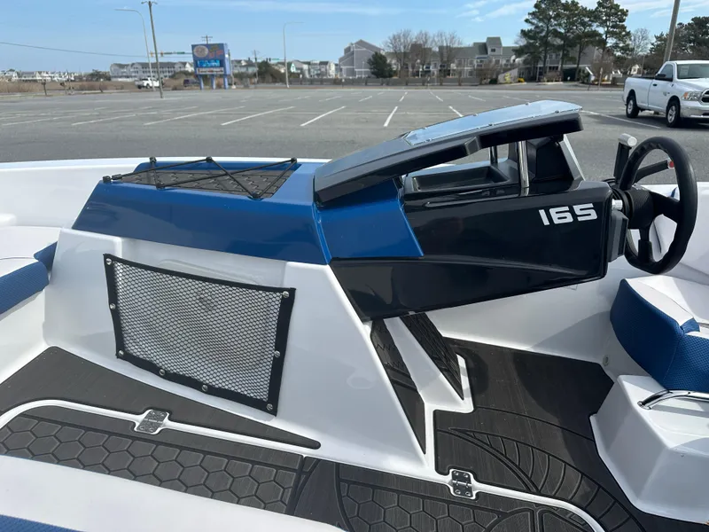 Slide: The Image of 2023 Scarab 165ID boat interior with steering wheel and dashboard in a parking lot. - 16