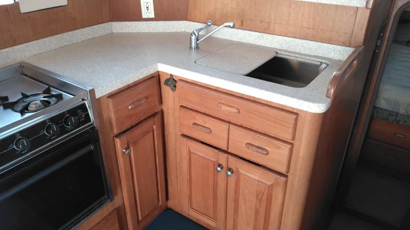 Slide: The Image of 1999 Mainship 350 Trawler kitchen with stove, sink, and wooden cabinets. - 29