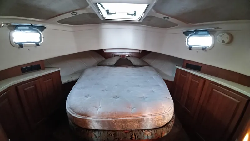 Slide: The Image of 1999 Mainship 350 Trawler cabin with bed, wooden cabinets, and porthole windows. - 30
