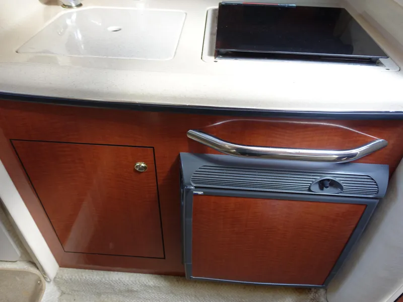 Slide: The Image of 2004 Sea Ray 280 Sundancer kitchenette with sink, stove, and wooden cabinetry. - 17