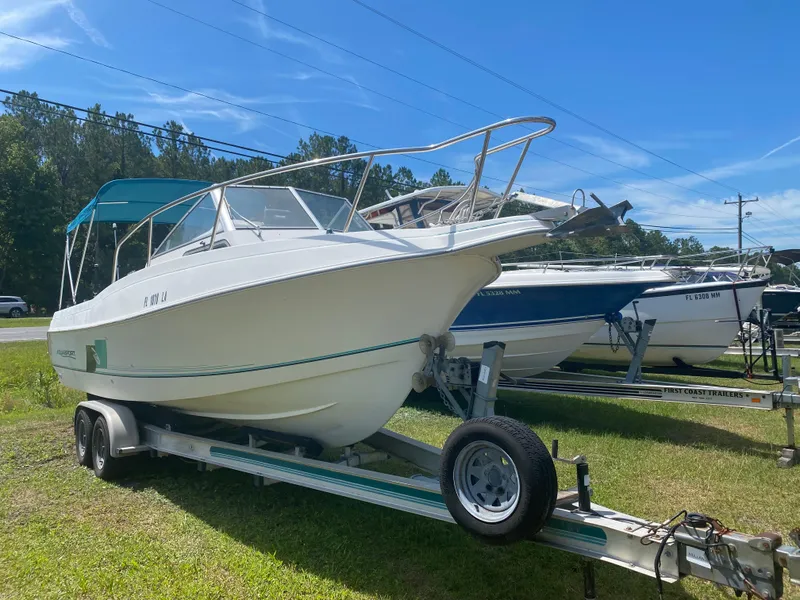 The Image of 1999 Aquasport 245 Explorer boat on a trailer in a grassy area. - 1